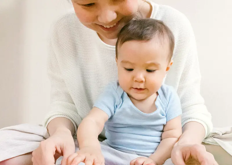 Smiling woman and baby on a colorful foam play mat, looking at a toy book together