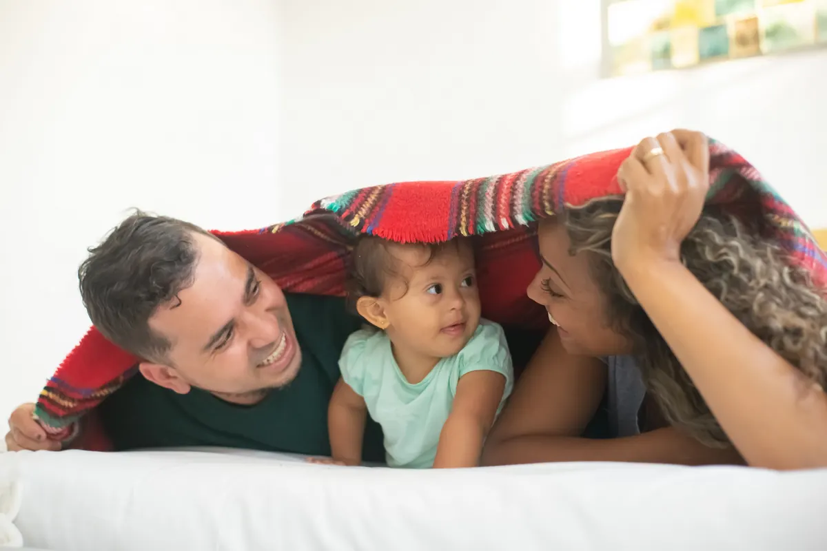 Two adults and a baby smiling under a red plaid blanket