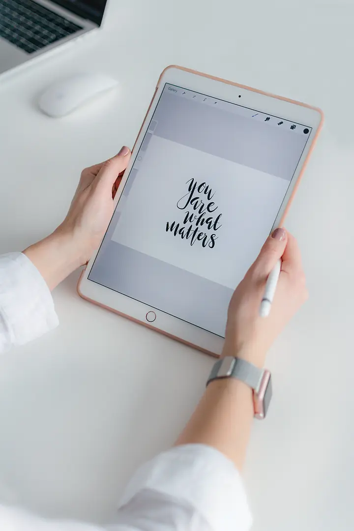 Hands holding a tablet over a bright white desk, showing the hand-lettered words “you are what matters”